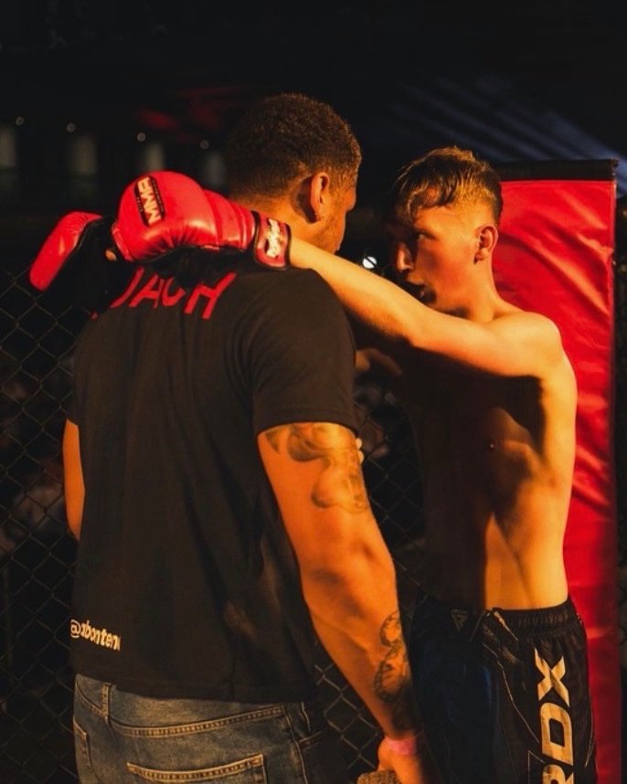 An Abonten coach with his arm round a fighter, talking him through it cageside