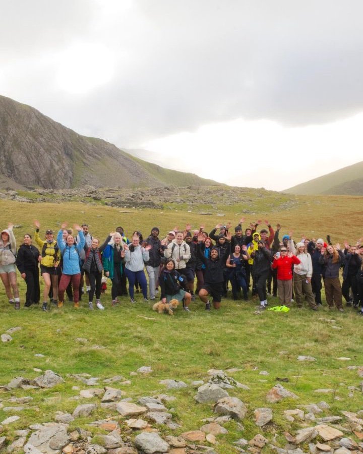A big Abonten group waving at the camera on the hike up Snowdon, mountains behind them