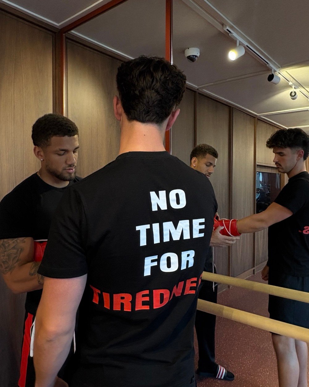 An Abonten coach wrapping a member's hands before a session, other members in No Time For Tiredness shirts getting ready