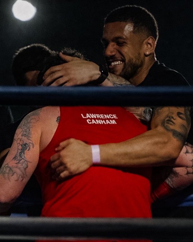 An Abonten coach hugging a boxer in a red vest at ringside after his bout